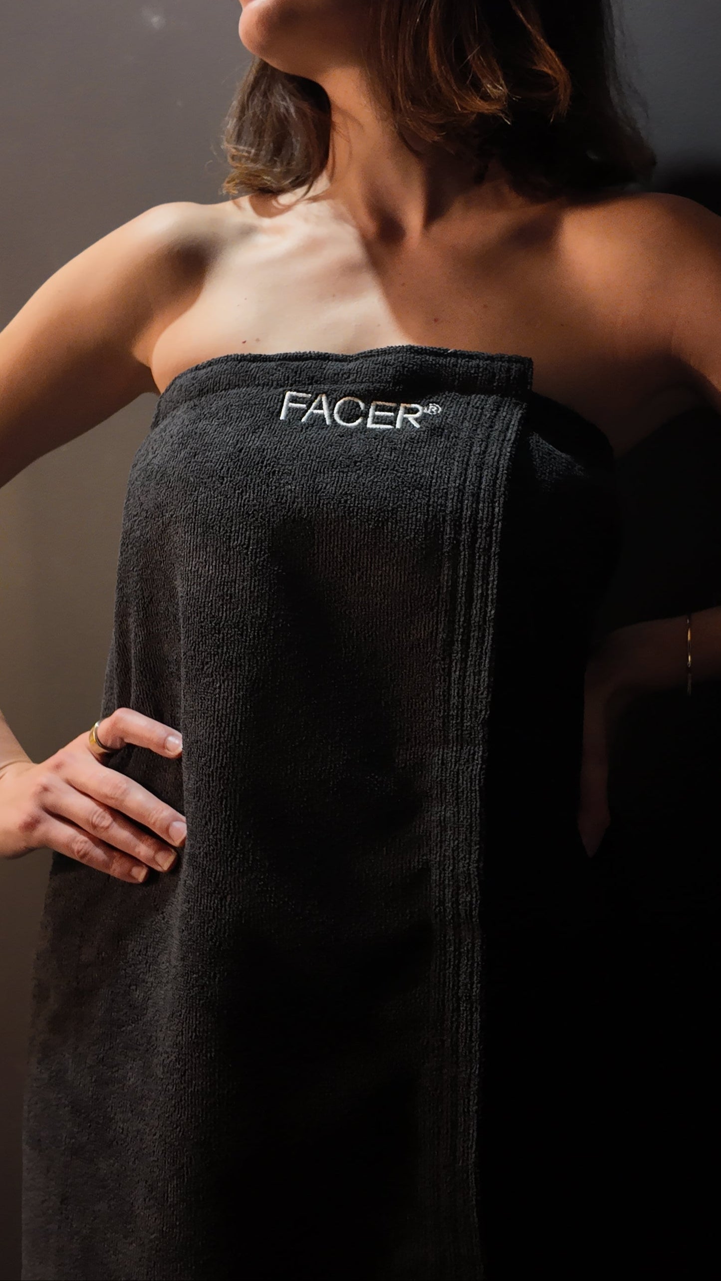 Woman wearing a black towel with 'FACER' branding against a neutral background